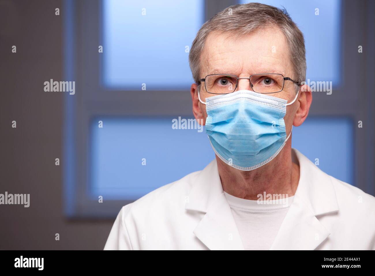 Portrait eines reifen Arztes mit OP-Maske und weißer Kleidung Blick auf die Kamera - Fokus auf die Augen Stockfoto