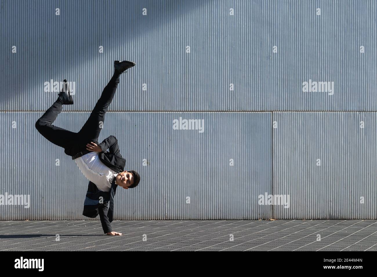 Asiatische männliche Unternehmer in formellen Anzug zeigt Breakdance Bewegung und Balancieren auf Arm im Handstand auf der Stadtstraße beim Schauen Bei der Kamera Stockfoto