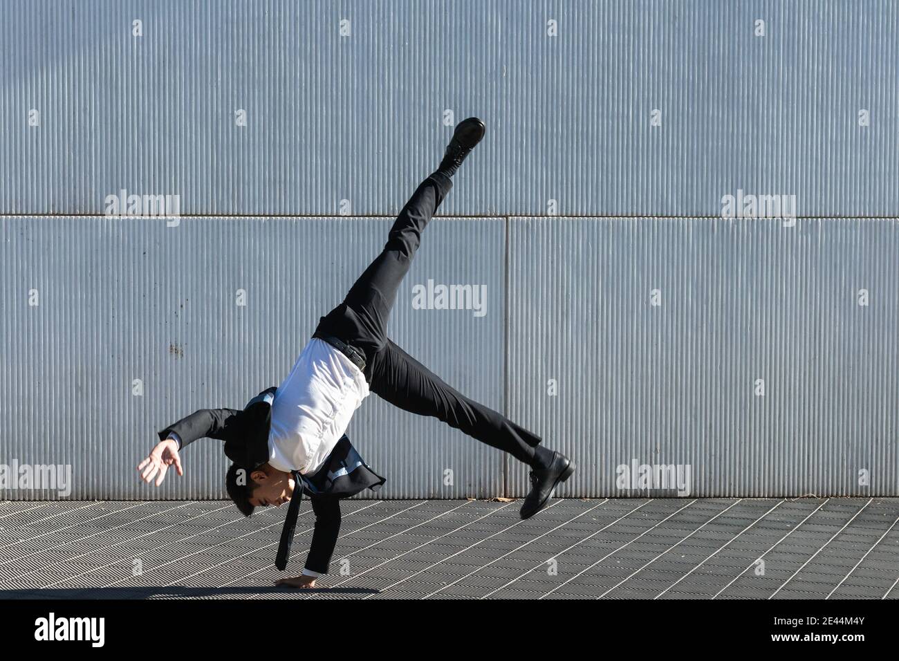 Asiatische männliche Unternehmer in formellen Anzug zeigt Breakdance Bewegung und Balancieren auf Arm im Handstand auf der Stadtstraße beim Schauen Bei der Kamera Stockfoto