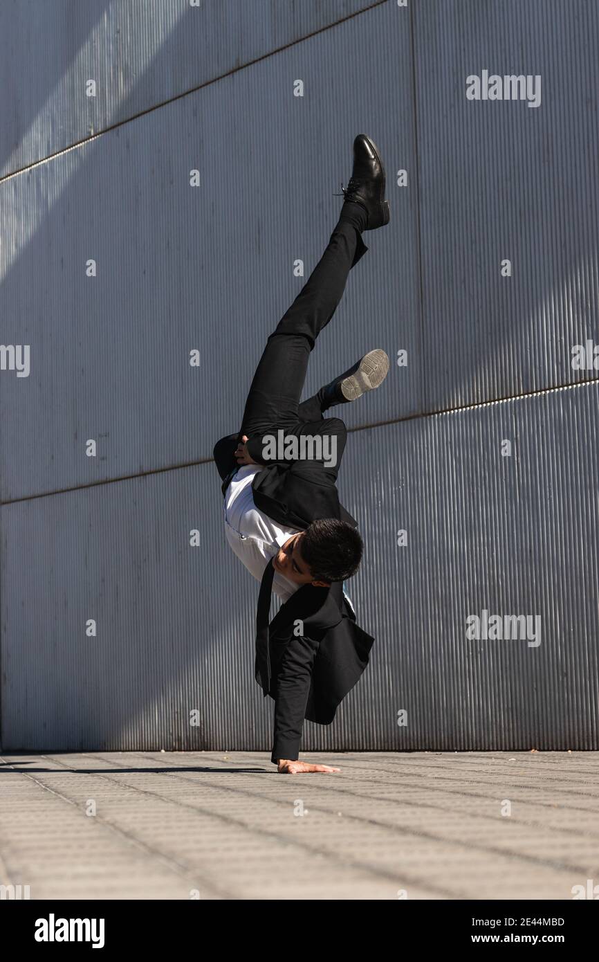 Asiatische männliche Unternehmer in formellen Anzug zeigt Breakdance Bewegung und Balancieren auf Arm im Handstand auf der Stadtstraße beim Schauen Bei der Kamera Stockfoto