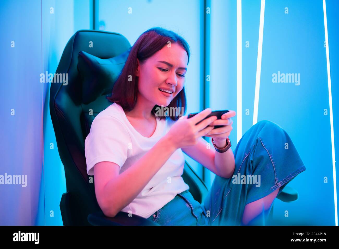 Cybersport Gamer spielen mobile Spiel auf dem Smartphone sitzen auf einem Gaming-Stuhl in Neon-Farbraum. Stockfoto