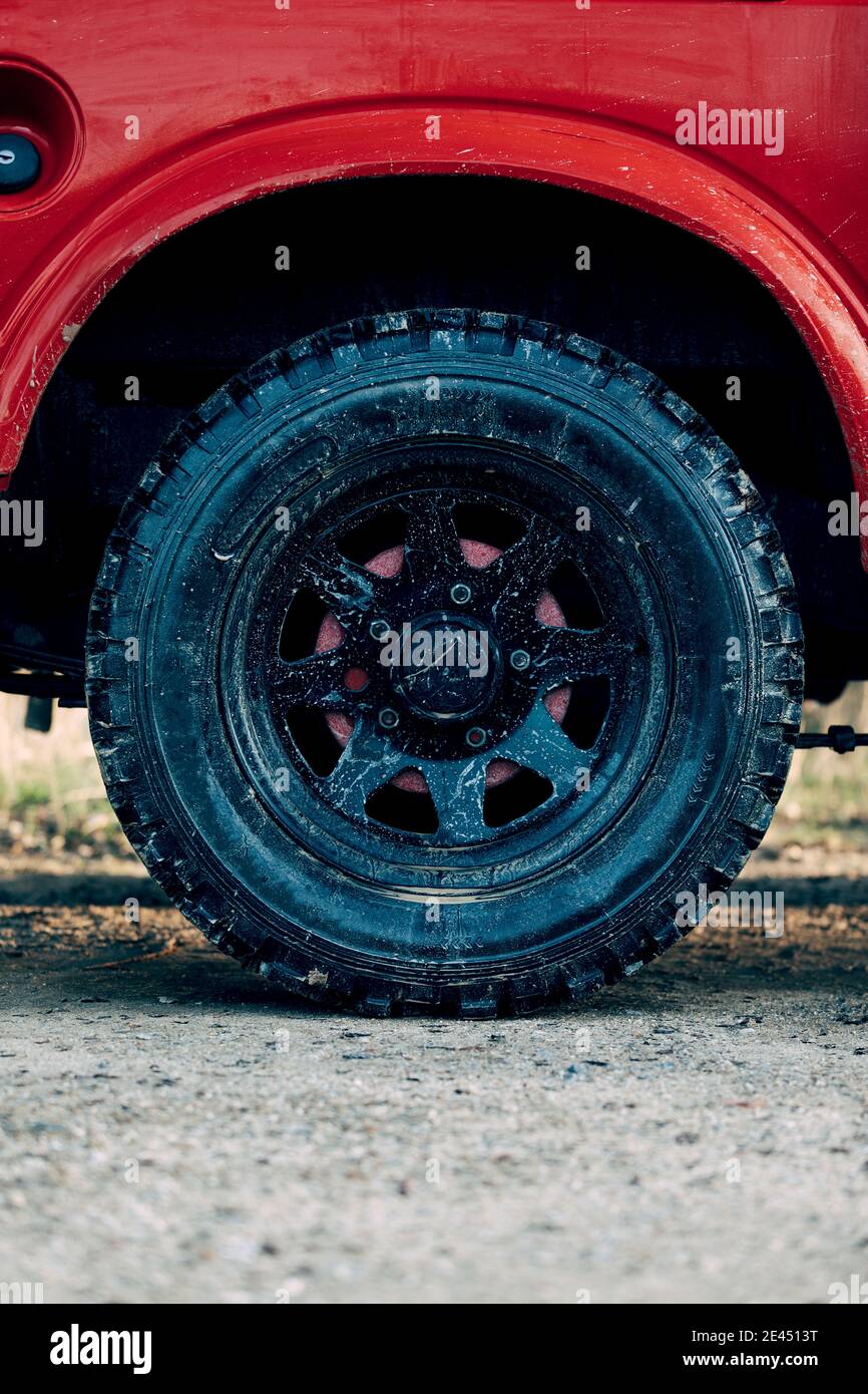 Rotes SUV-Fahrzeug mit schwarzen Reifen auf Schmutz geparkt Straße während Abenteuer auf dem Land Stockfoto