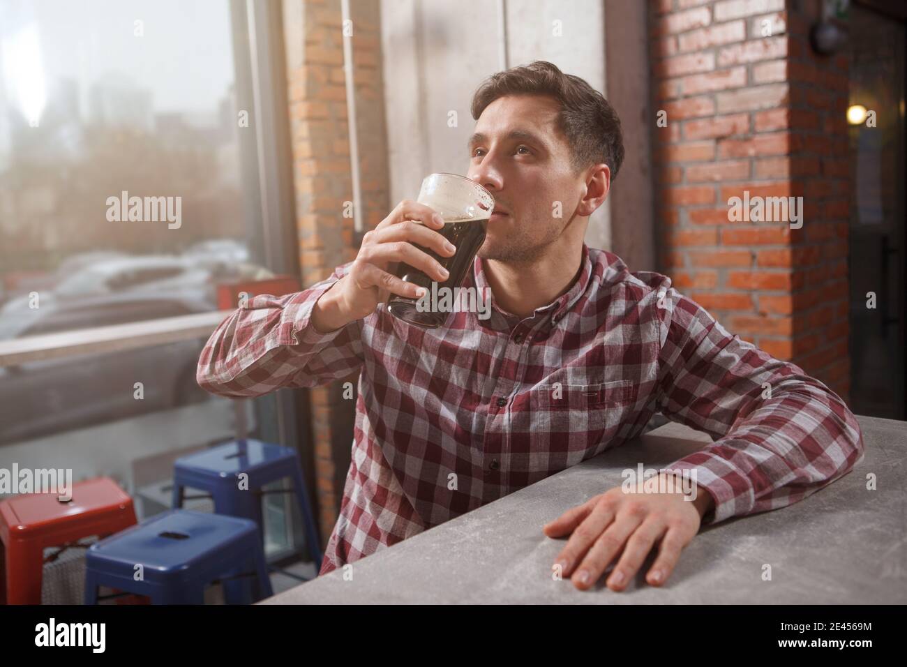 Junger Mann schlürft köstliches Craft-Bier, entspannt im Bierkneipe, Copy Space Stockfoto