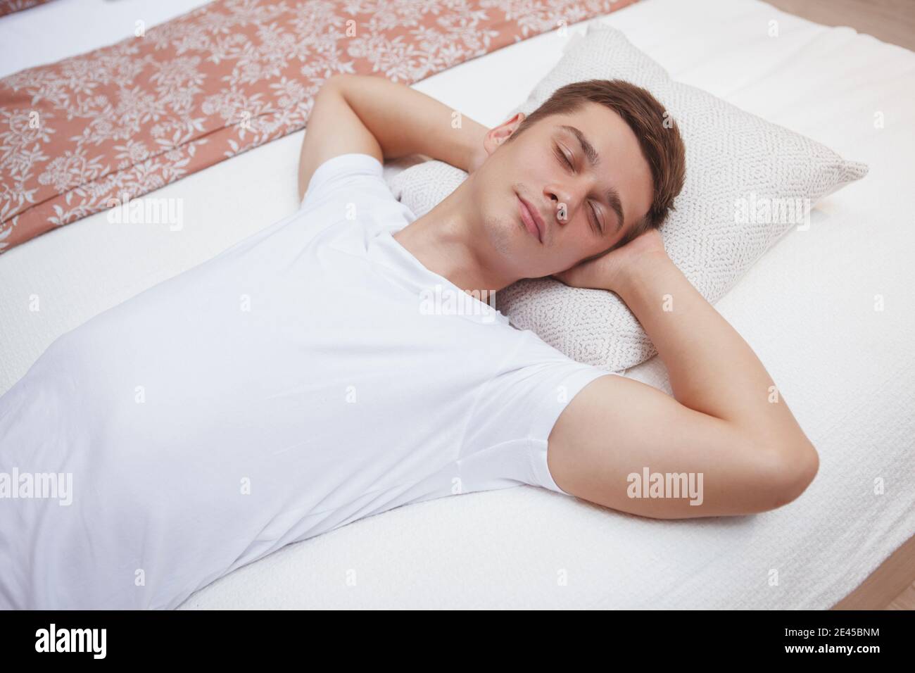 Junger Mann, der auf einem Bett schläft, sieht entspannt und ruhig aus Stockfoto