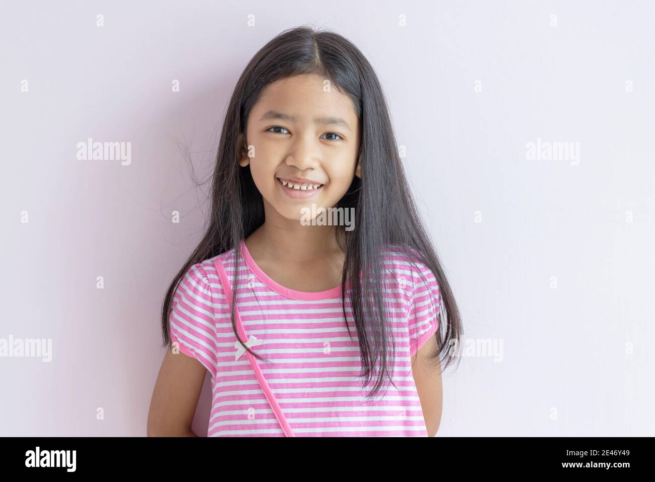 Asiatische kleine Mädchen lächeln hell. Kinder tragen rosa Kreuz weiße Kleider und lange schwarze Haare. Das Kind schaut nach vorne und lächelt fröhlich. Porträts Stockfoto