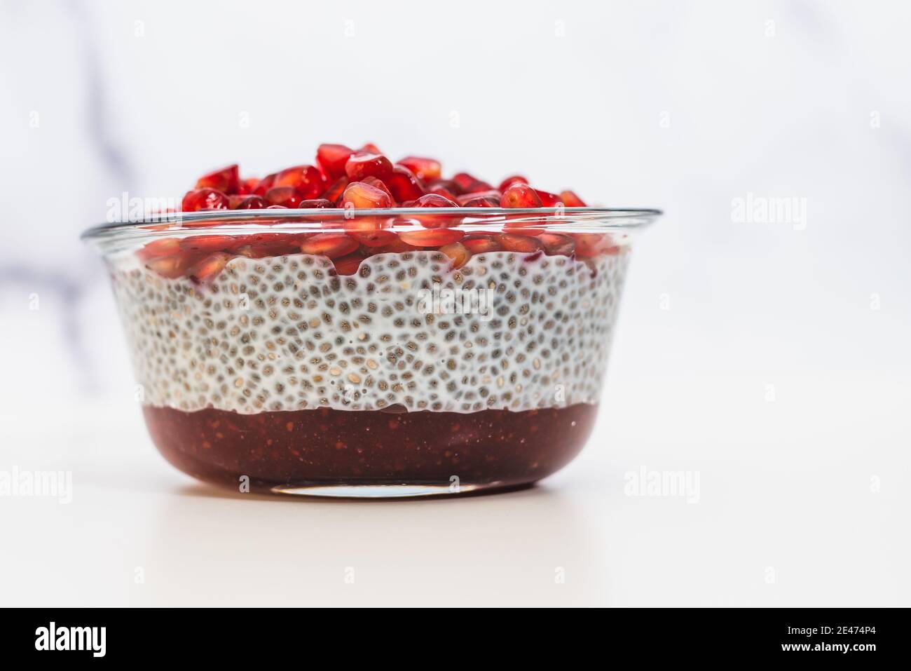 Chia-Samenpudding mit Himbeermarmelade und Granatapfelkernen Glasschale Nahaufnahme auf weißem Hintergrund Stockfoto