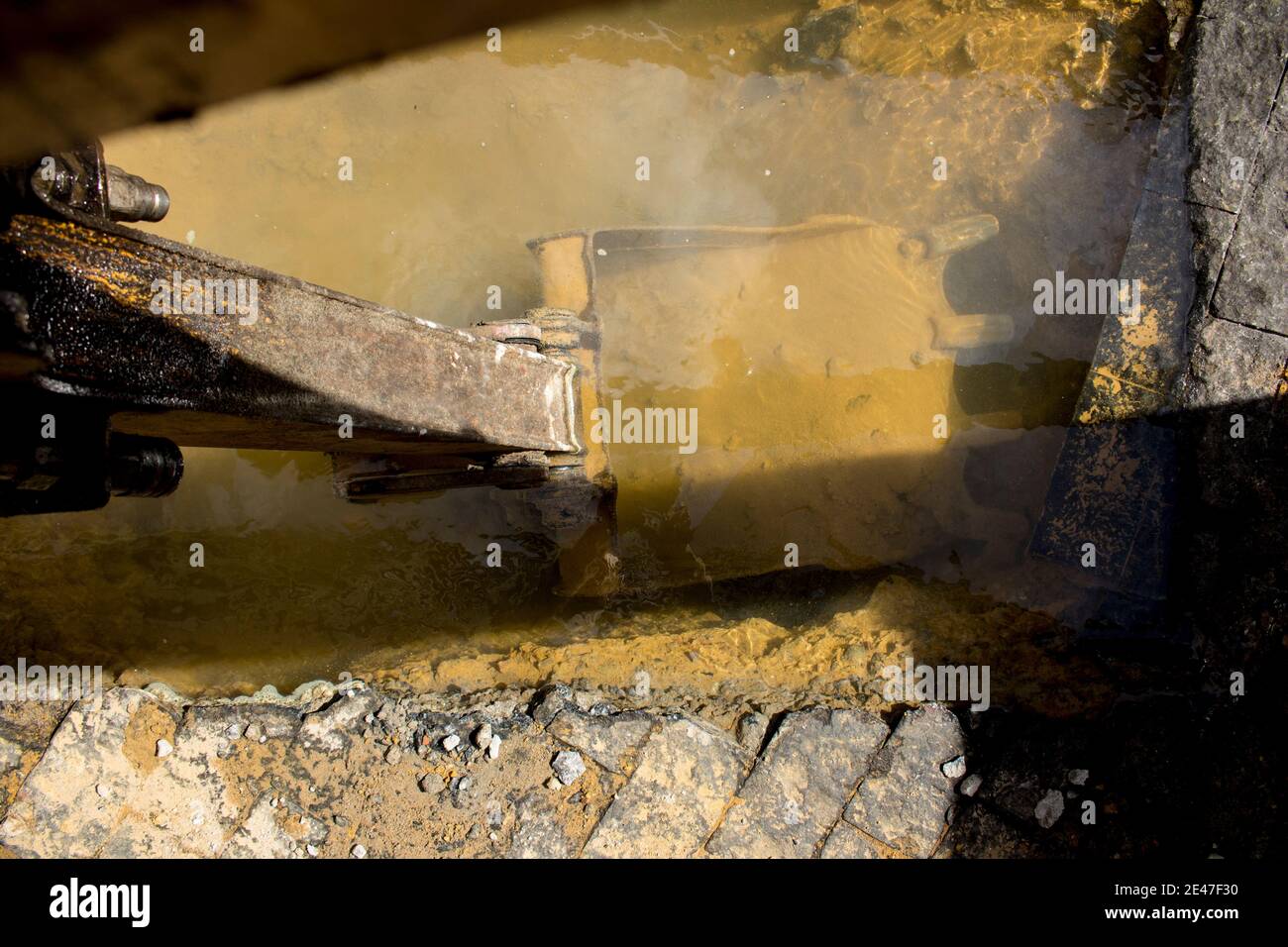 Rostiger Bagger schaufeln unter schmutzigem Wasser bei dem Loch von Die Kanalisation in der Straße Stockfoto