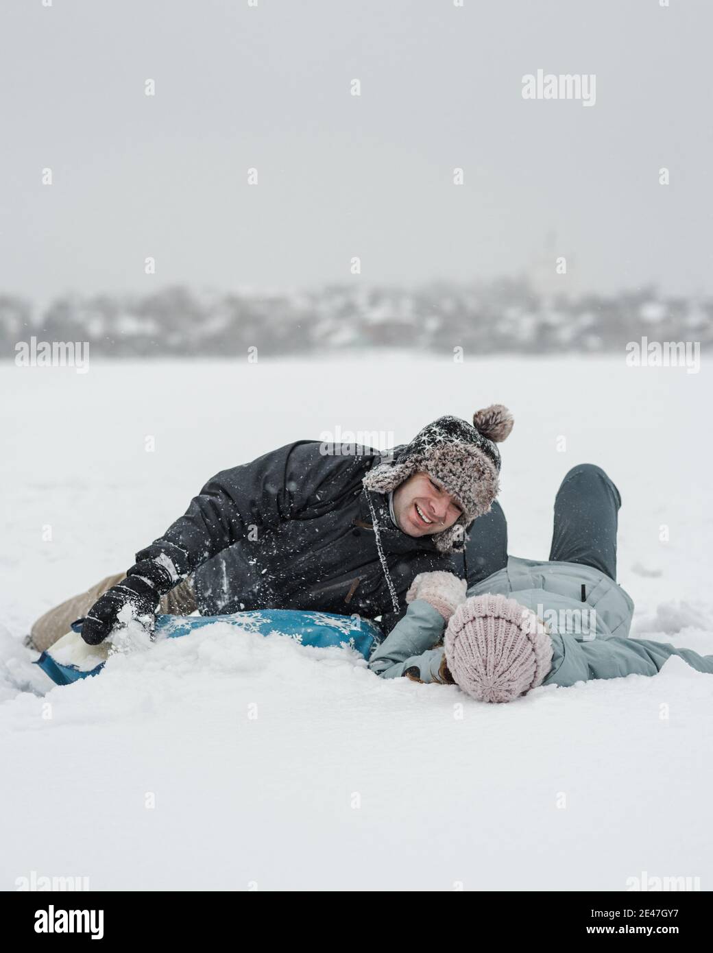 Mann mit Freundin, die in die Schneeröhre fällt. Junge glückliches Paar zu Fuß im Wintertag Stockfoto