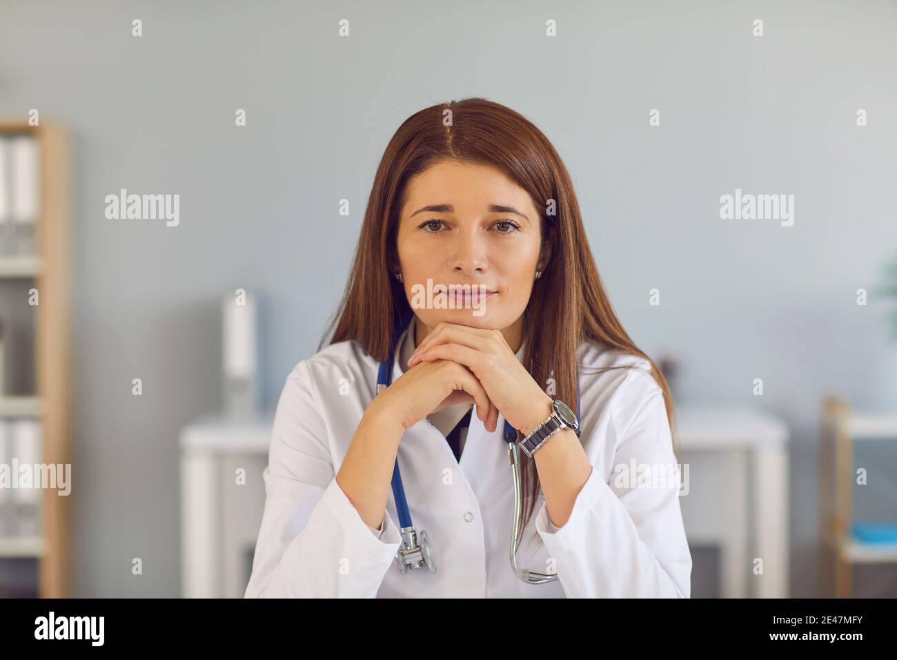 Porträt einer jungen müden rothaarigen Ärztin, die am Tisch sitzt und sich an ihre Hände lehnt. Stockfoto