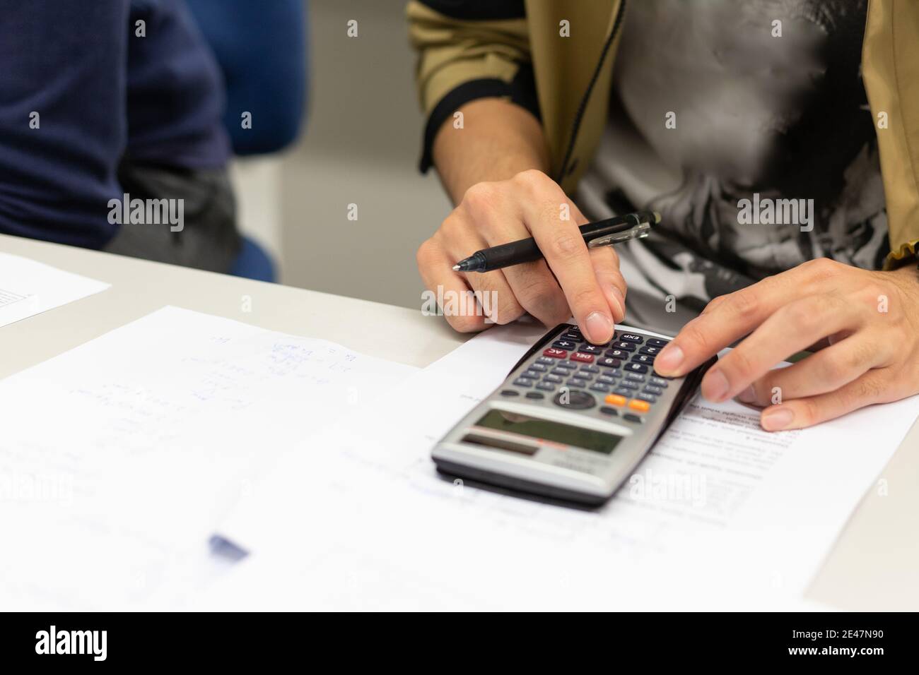 Nahaufnahme der Hände des männlichen Studenten mit Taschenrechner, Bleistift halten, um die Ergebnisse im Klassenzimmer in der Universität aufzuschreiben Stockfoto