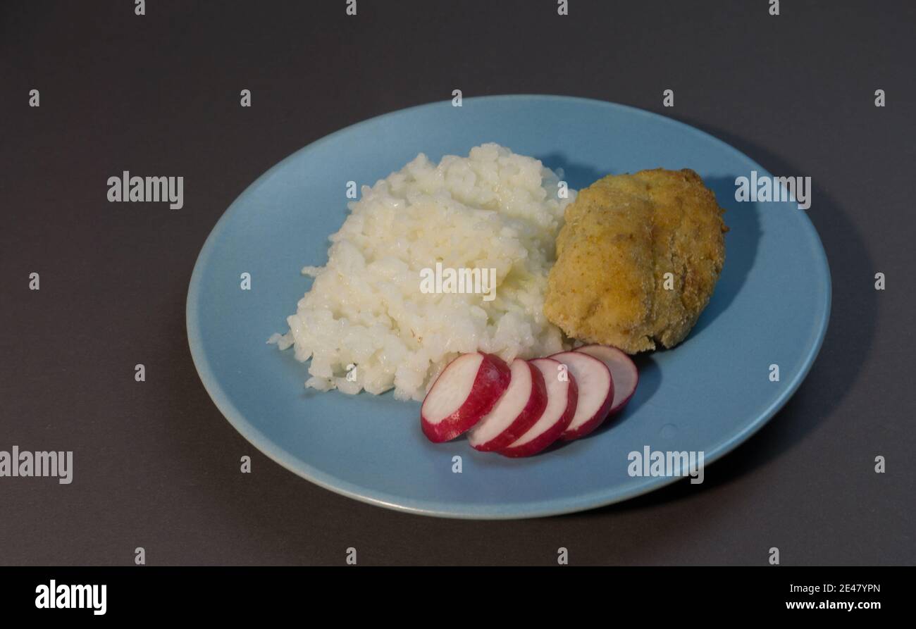 Gekochter weißer Reis mit Fischschnitzel in Speck auf einem grauen Hintergrund blauen Teller eingewickelt. Fischball mit Reisgarnieren und Rettich. Stockfoto