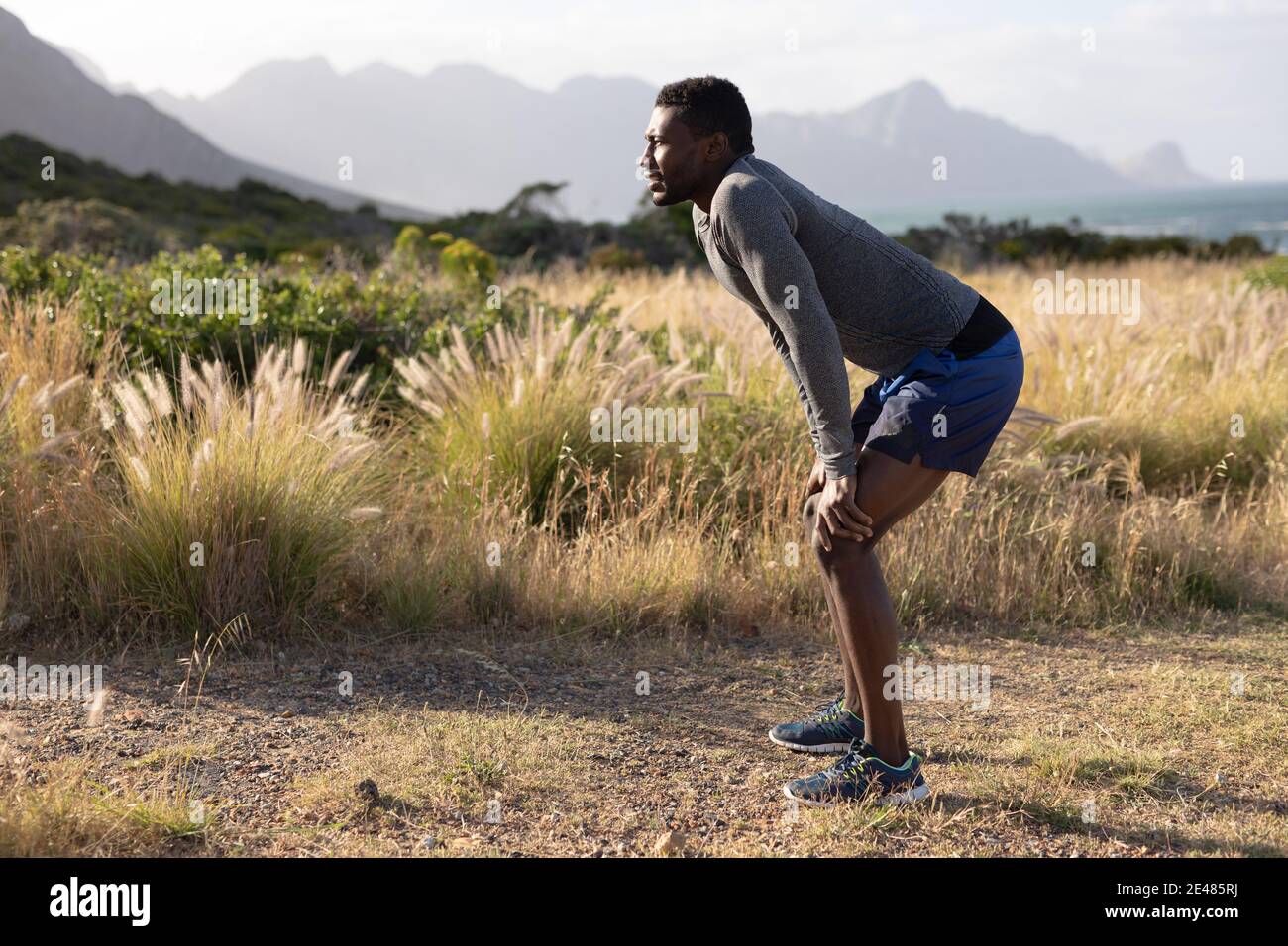 Fit afroamerikanischen Mann in Sportbekleidung auf den Knien lehnen Im hohen Gras Stockfoto