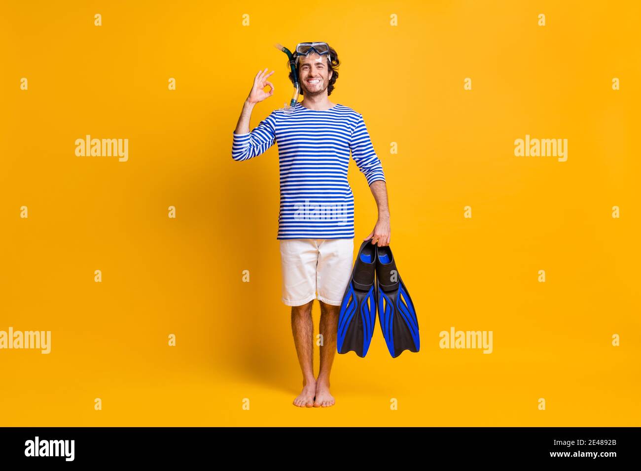 In voller Länge Foto von barfuß Kerl halten Schnorcheln Flossen zeigen Okay Zeichen tragen Maske Brille isoliert über gelbem Hintergrund Stockfoto