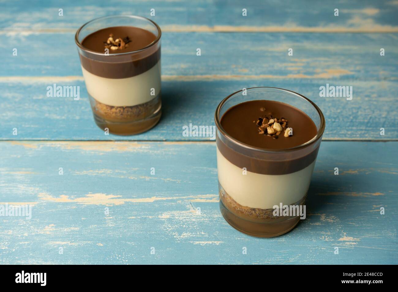 Zwei Schokoladendessert in Glas (Joghurt oder Sahne, Kekse und Nüsse) Süßigkeiten süßes Konzept auf blauem Sommer Holzhintergrund. Stockfoto
