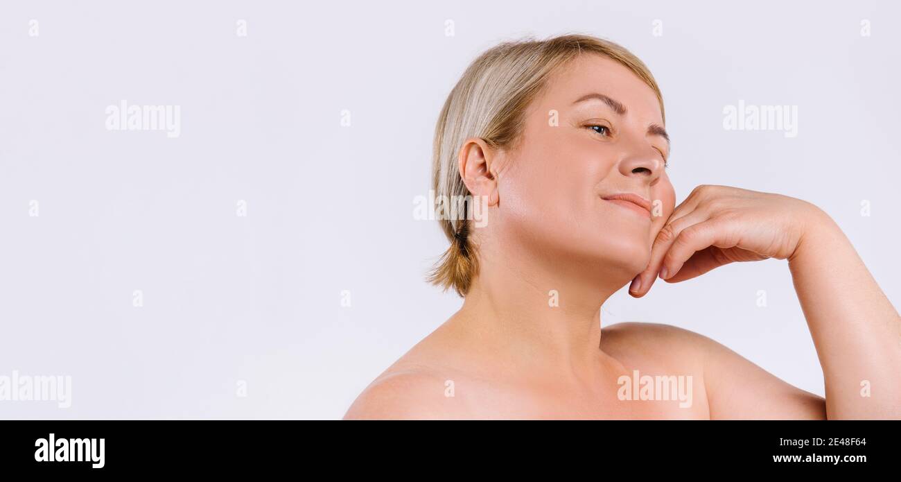 Banner. Ältere Frau mit feuchtigkeitsspendender Haut nach kosmetischen Verfahren lächelt und schaut zur Seite, sanft berühren die Haut ihres Gesichts. Weiß Stockfoto
