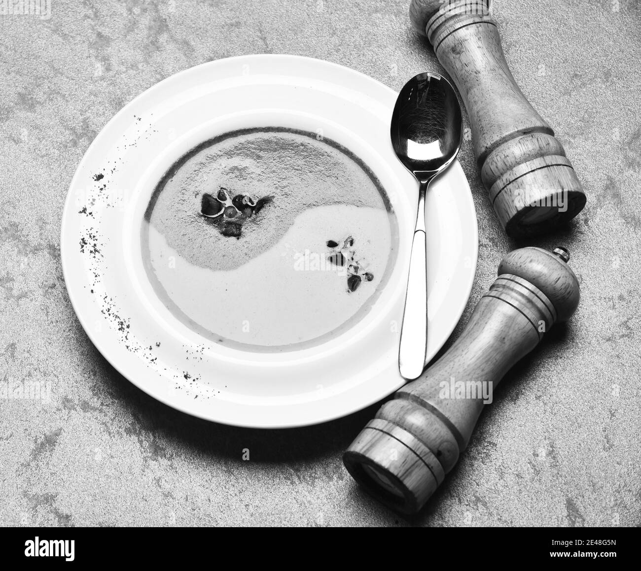 Püree in grüner und gelber Farbe in Yin Yang Zeichen durch Pfefferbox, Salzkeller und Löffel. Traditionelles Küchenkonzept. Spinat- und Kürbiscremesuppe auf grauem Texturhintergrund. Japanische Suppe im Restaurant. Stockfoto