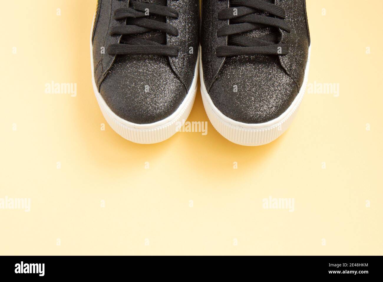 Schwarze Sneakers auf hellgelbem Hintergrund. Konzept des gesunden Lebensstils, tägliches Training. Schuhe für Damen-Training. Flach liegend Stockfoto