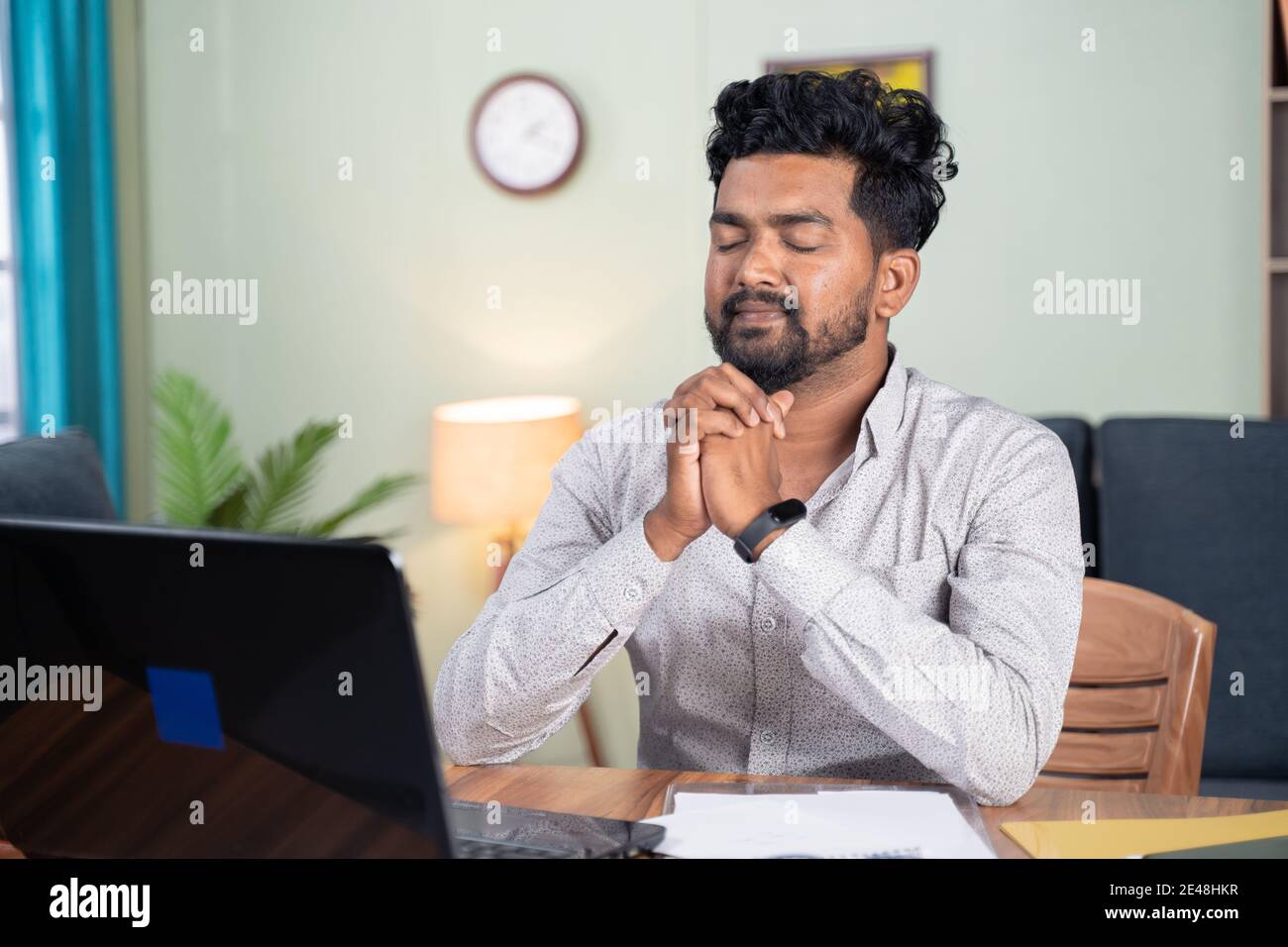 Junger Mann, der vor dem Laptop betet, nachdem er fertig ist Online-Test oder Prüfung für Ergebnisse - Konzept der glauben Und Dankbarkeit Stockfoto