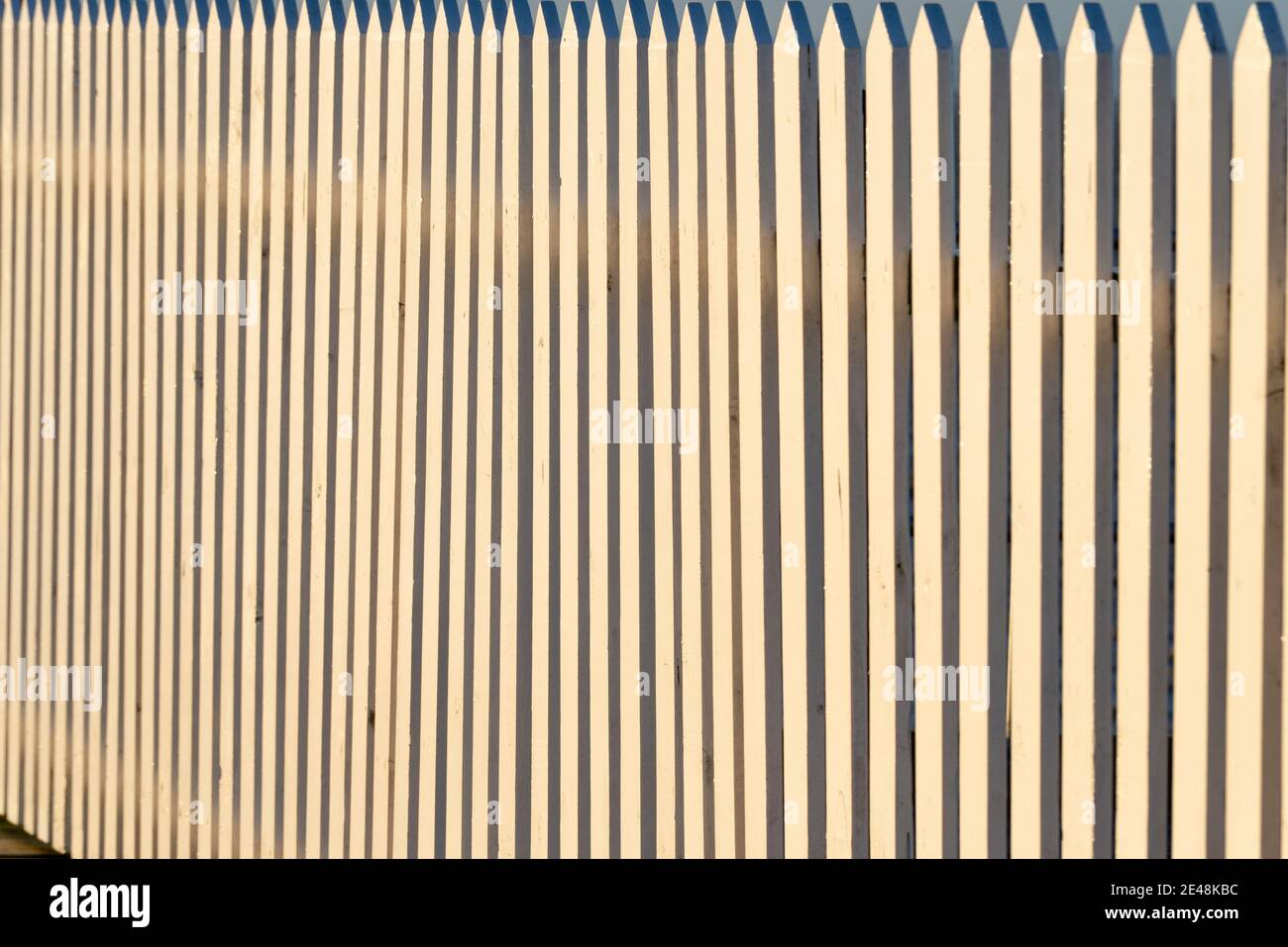 Weißer hölzerner Pfostenzaun mit Orange bei Sonnenaufgang. Vertikale Holzplatten. Traditionelle Grenzzäunung Stockfoto
