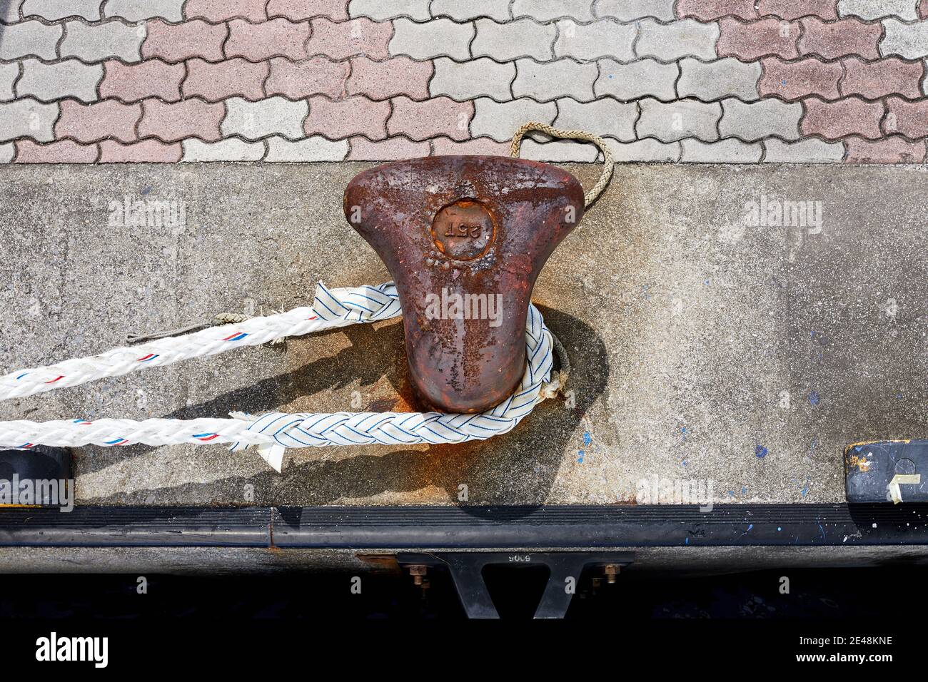 Hawser um einen rostigen Poller auf einem Betonkai Stockfoto