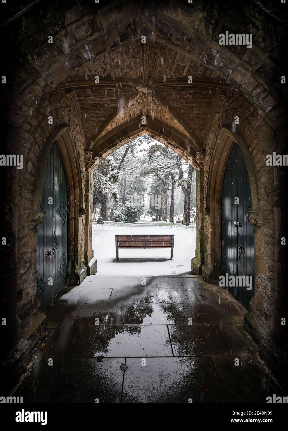 Winter Kirchhof Grabhof mit einsamer Bank im fallenden Schnee Winterszene Torbogen schöne und friedliche Decke Schneefall Nottinghamshire Friedhof Stockfoto