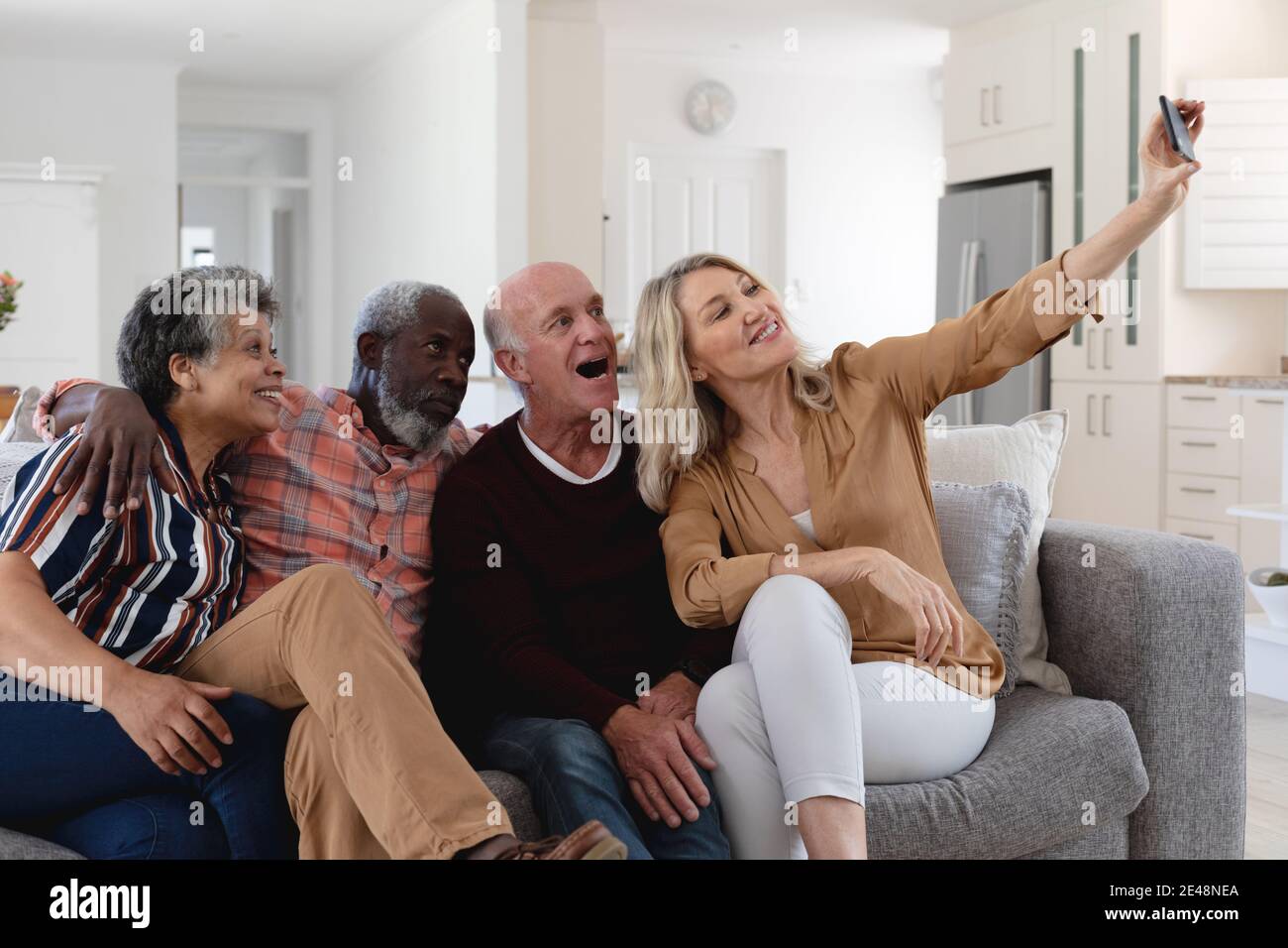 Ältere kaukasische und afroamerikanische Paare, die auf der Couch sitzen Ein Selfie zu Hause Stockfoto