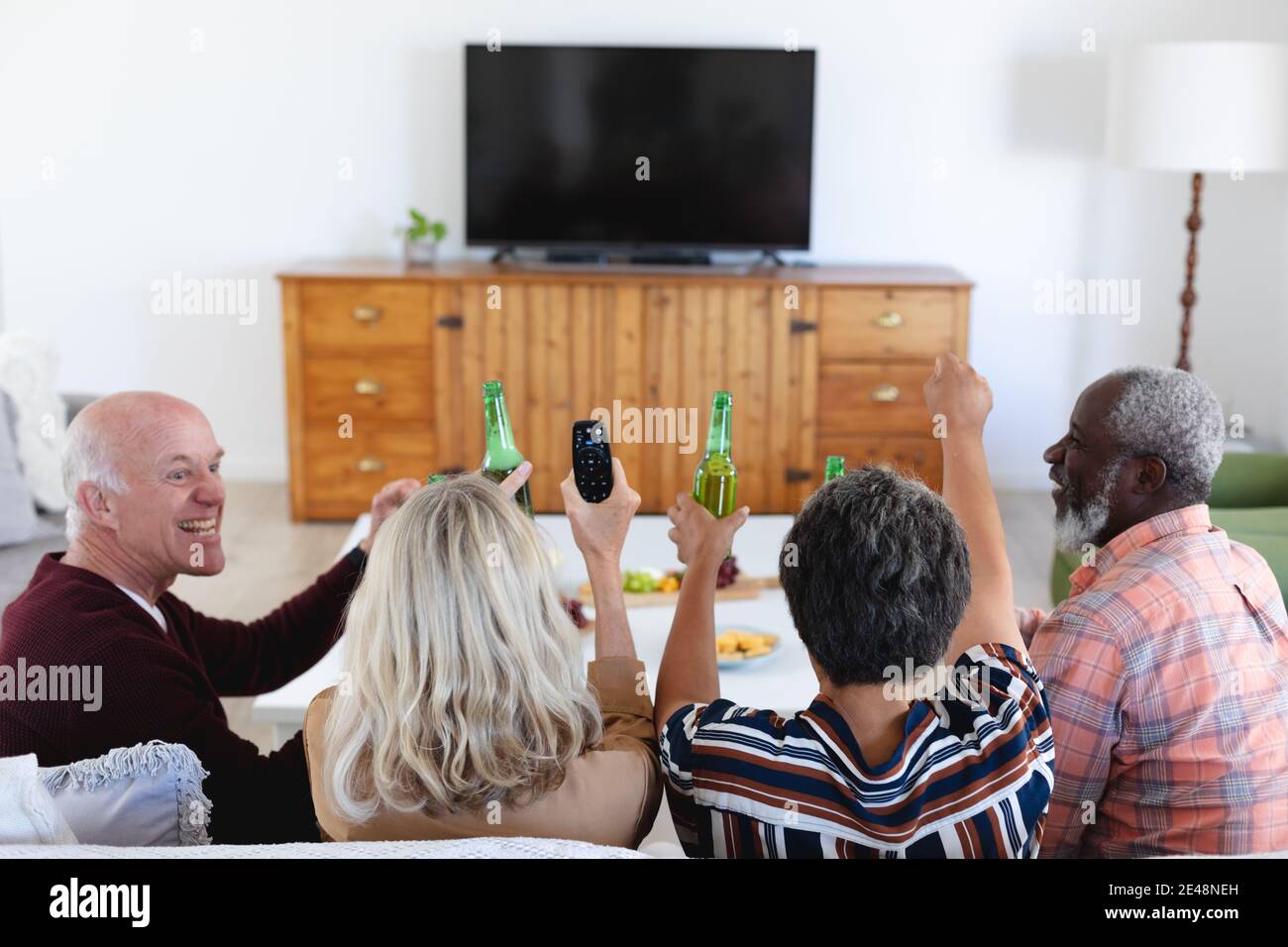 Ältere kaukasische und afroamerikanische Paare sitzen auf der Couch und beobachten Wild Bier zu Hause trinken Stockfoto