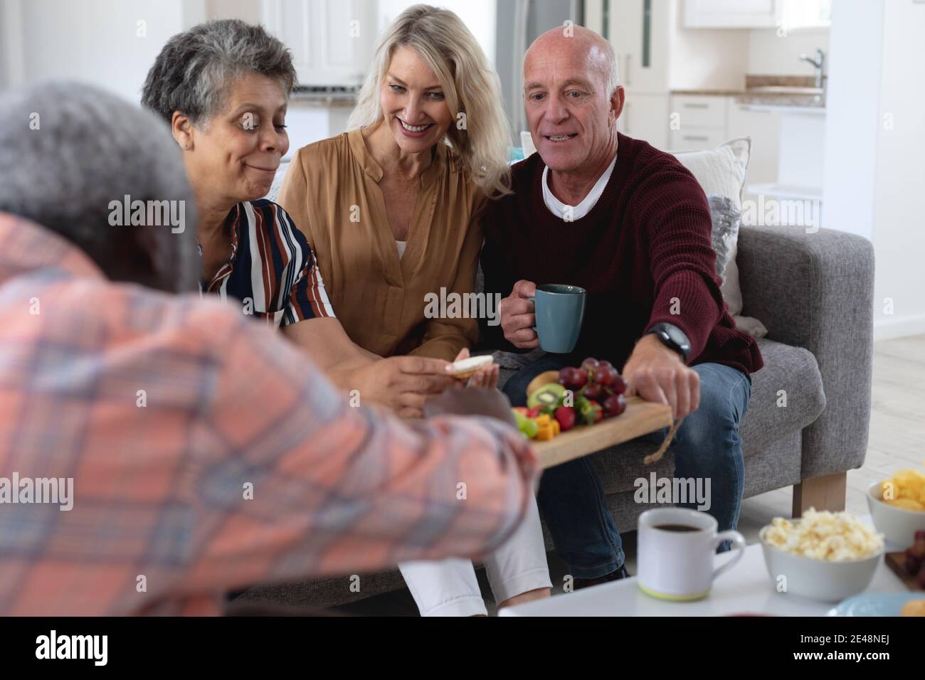 Ältere kaukasische und afroamerikanische Paare sitzen am Tisch beim Essen Käse und Obst zu Hause Stockfoto