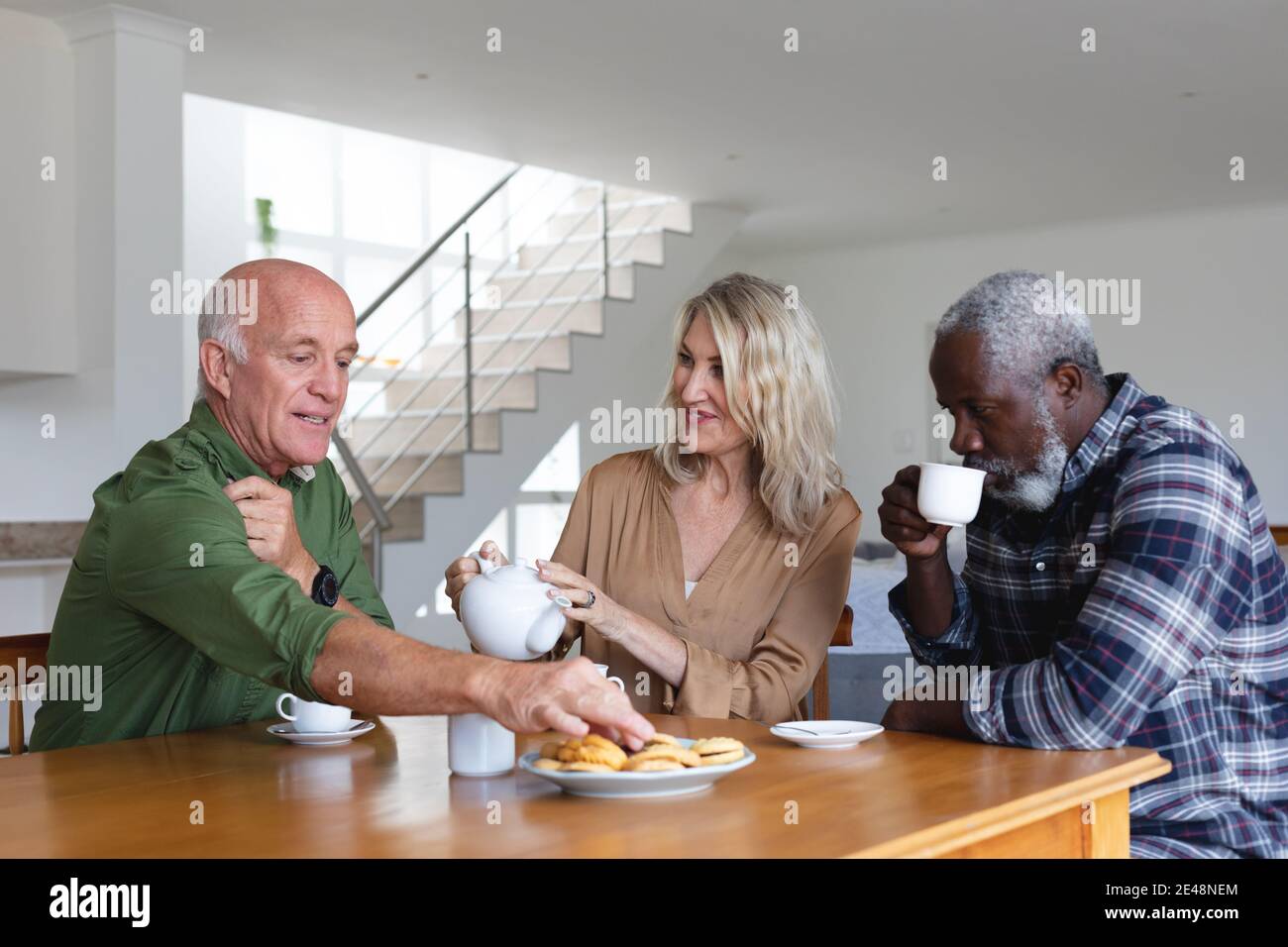 Ältere kaukasische und afroamerikanische Paare sitzen am Tisch und trinken Tee zu Hause Stockfoto