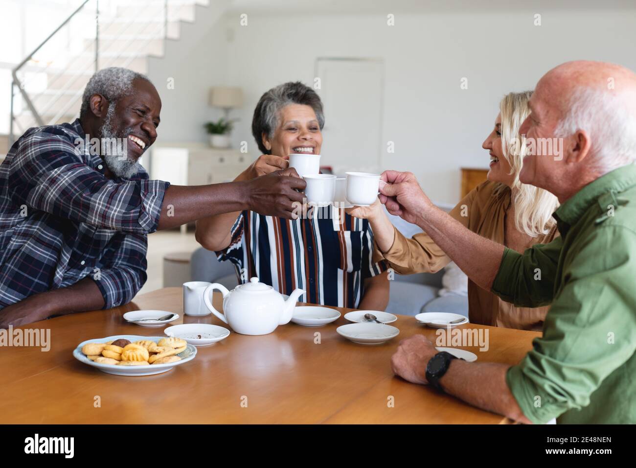 Ältere kaukasische und afroamerikanische Paare sitzen am Tisch und trinken Tee zu Hause Stockfoto