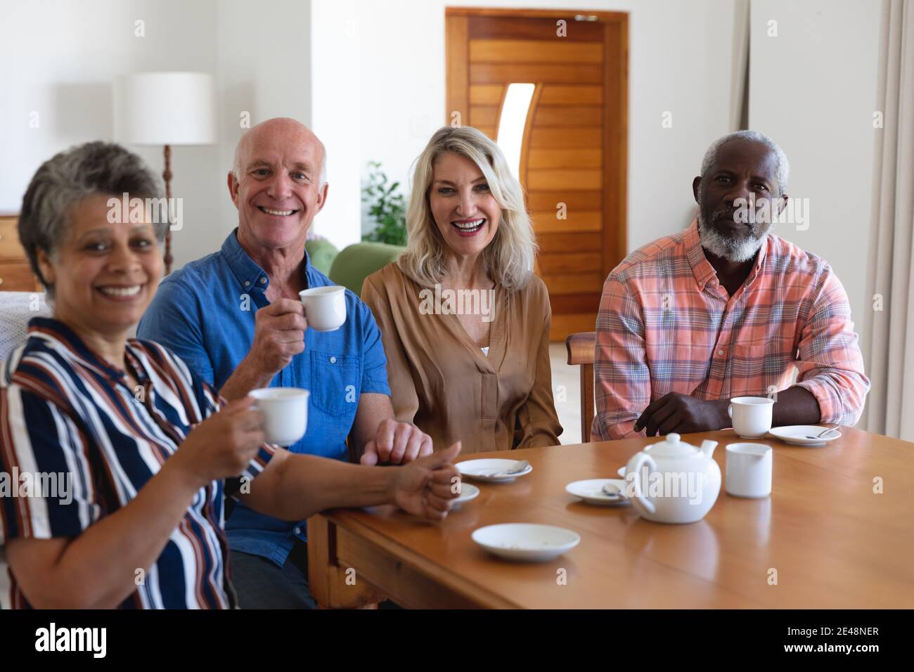 Ältere kaukasische und afroamerikanische Paare sitzen am Tisch und trinken Tee zu Hause Stockfoto