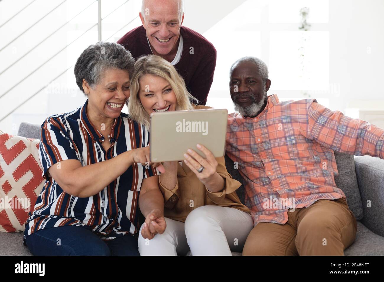 Ältere kaukasische und afroamerikanische Paare, die auf der Couch sitzen Digitales Tablet zu Hause Stockfoto
