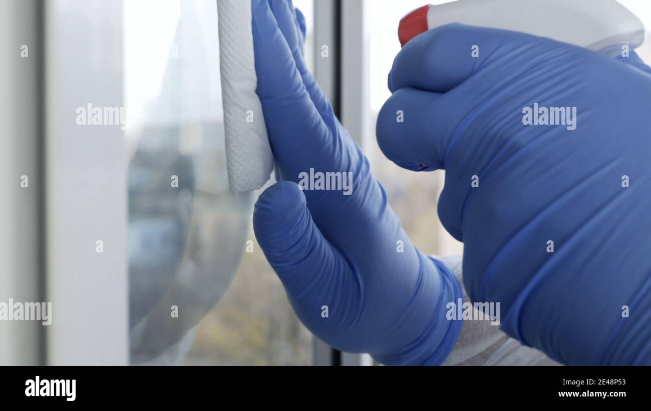 Nahaufnahme man Hände mit Schutzhandschuhe Reinigung eines Fensters mit gespritzten Flüssigkeit Desinfektion gegen Viren Kontamination Stockfoto