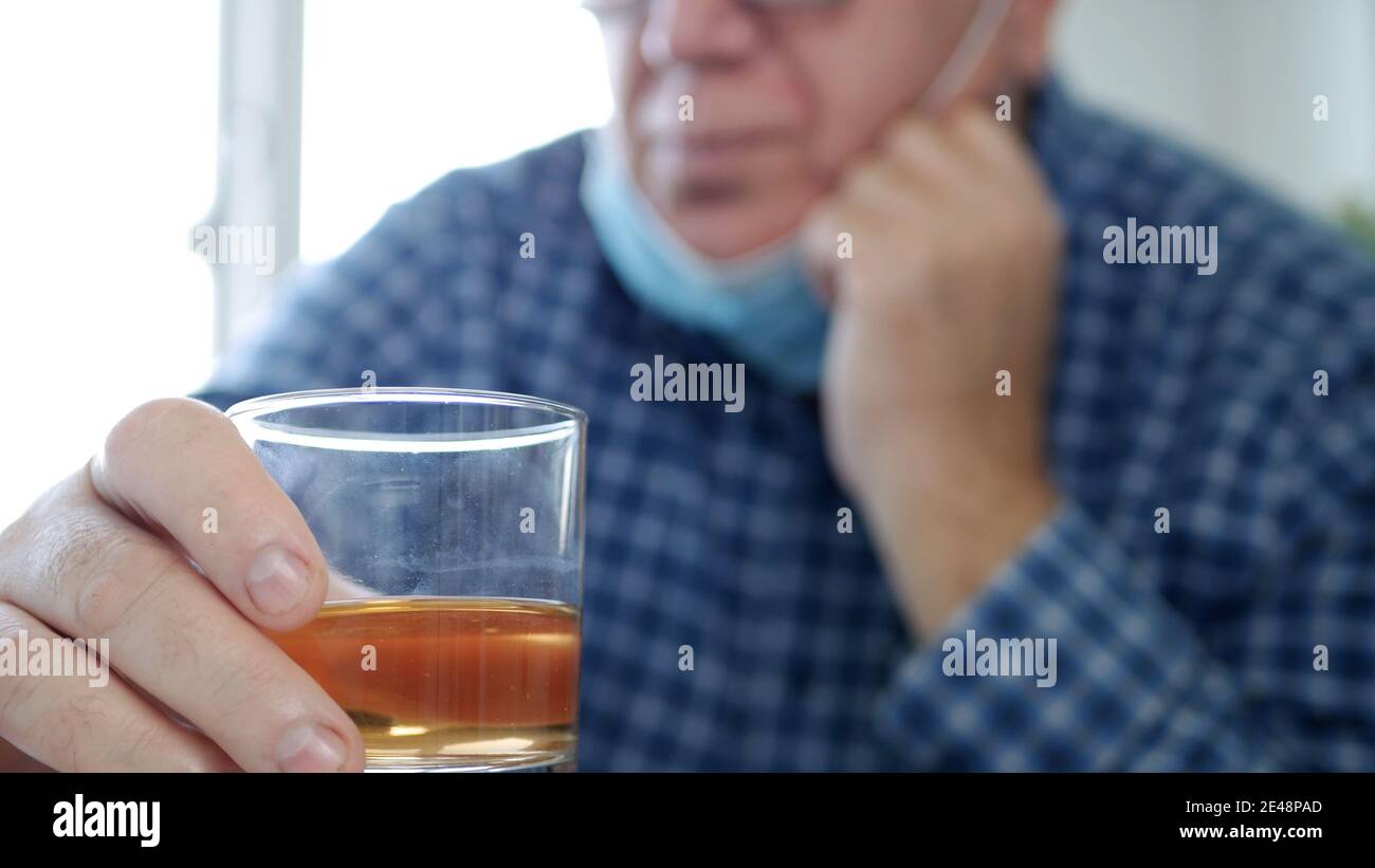 Betrunkener Mensch mit Schutzmaske auf seinem Gesicht trinkt ein Glas Alkohol in einer Bar Stockfoto