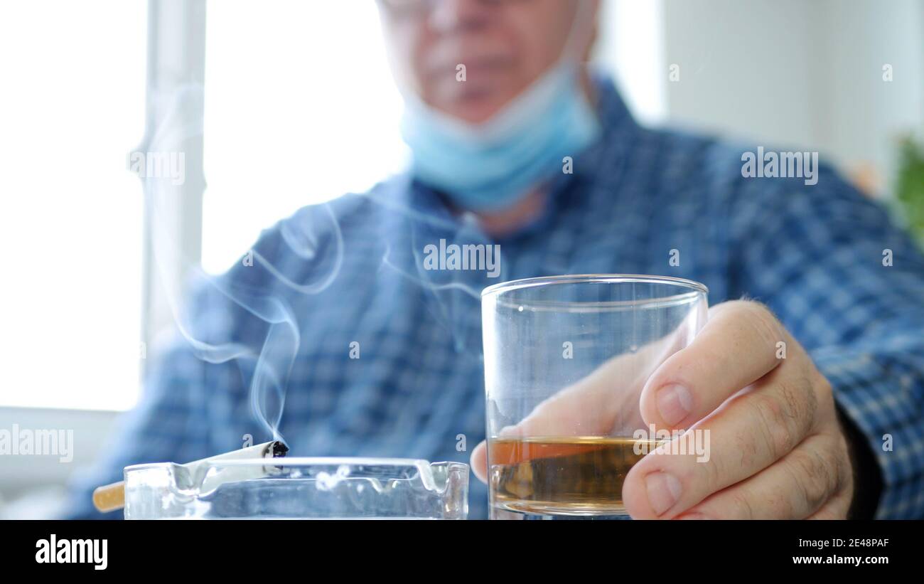 Mann trägt Schutzmaske auf seinem Gesicht trinken ein Glas mit Alkohol in einer Bar und rauchen eine Zigarette Stockfoto