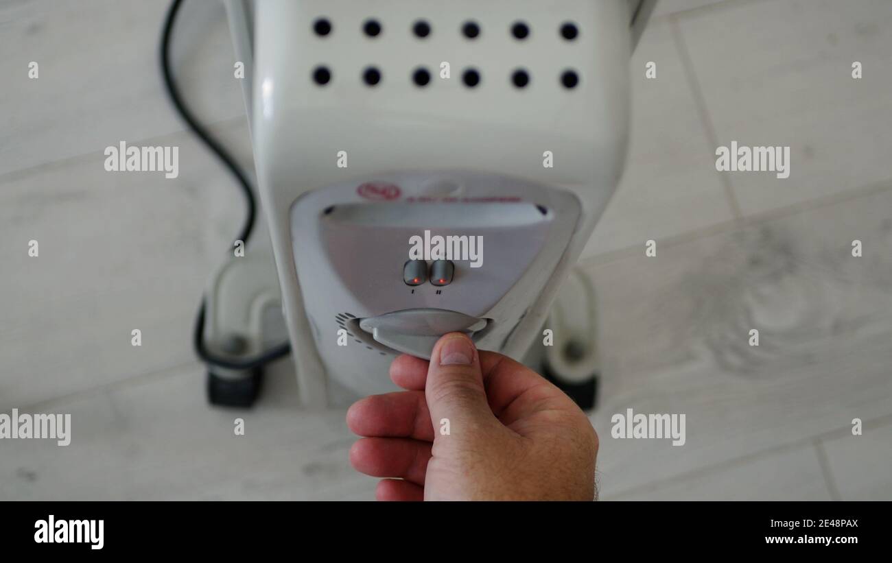 Man stellt die Heiztemperatur eines elektrischen Heizkörpers zu Hause in einem kalten Raum ein Stockfoto
