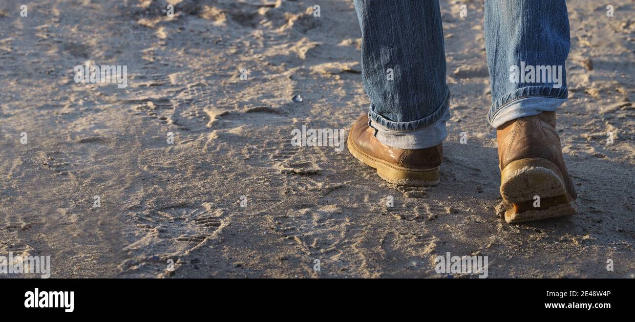 Mann, der auf Sand nach vorne geht, Füße mit Lederstiefeln und aufgerollten Jeans bewegt, Freizeitbeschäftigung oder Arbeitskonzept, ausgewählter Fokus, enge Tiefe Stockfoto