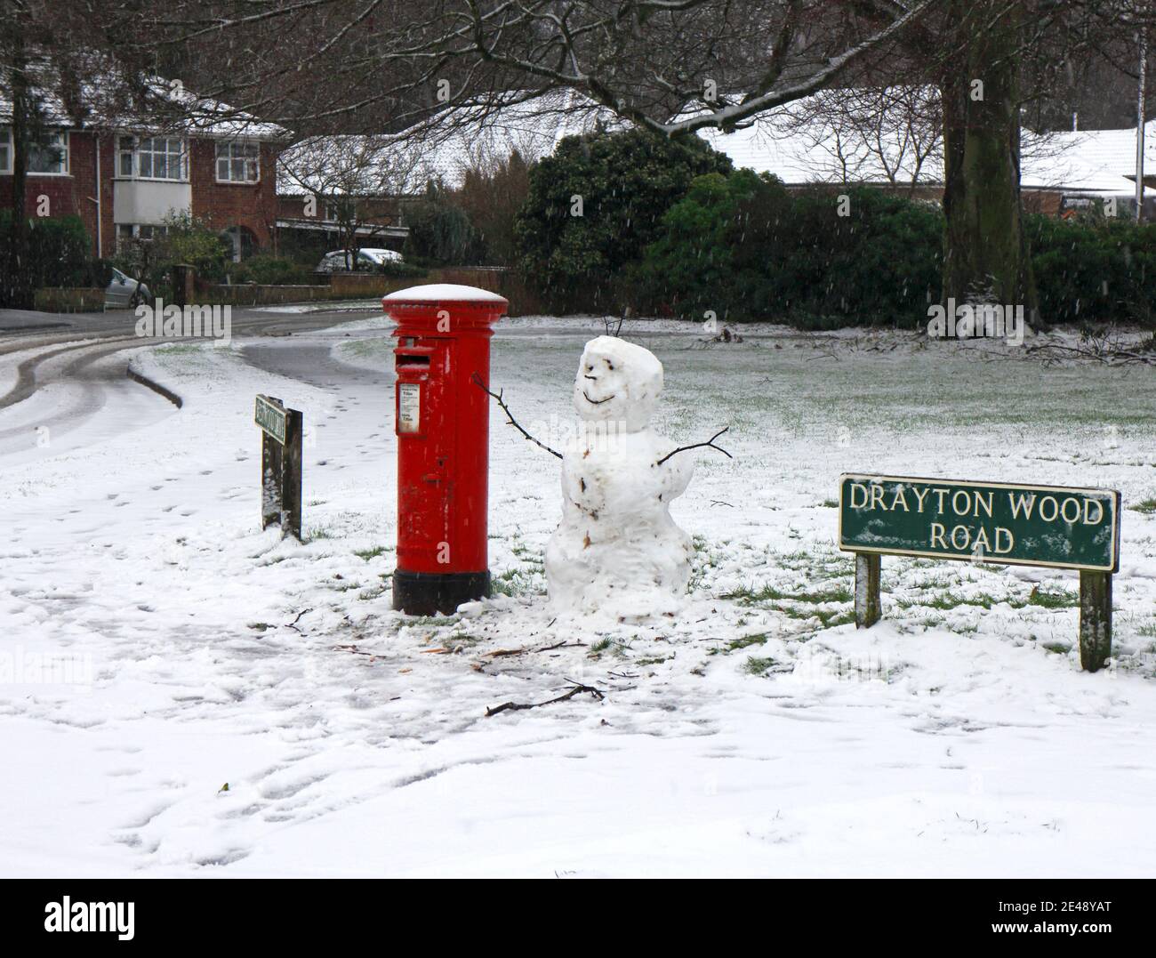 Ein Schneemann, der zwischen einem Straßenschild und einem roten Briefkasten in einem Wohngebiet von Hellesdon, Norfolk, England, Großbritannien, steht. Stockfoto