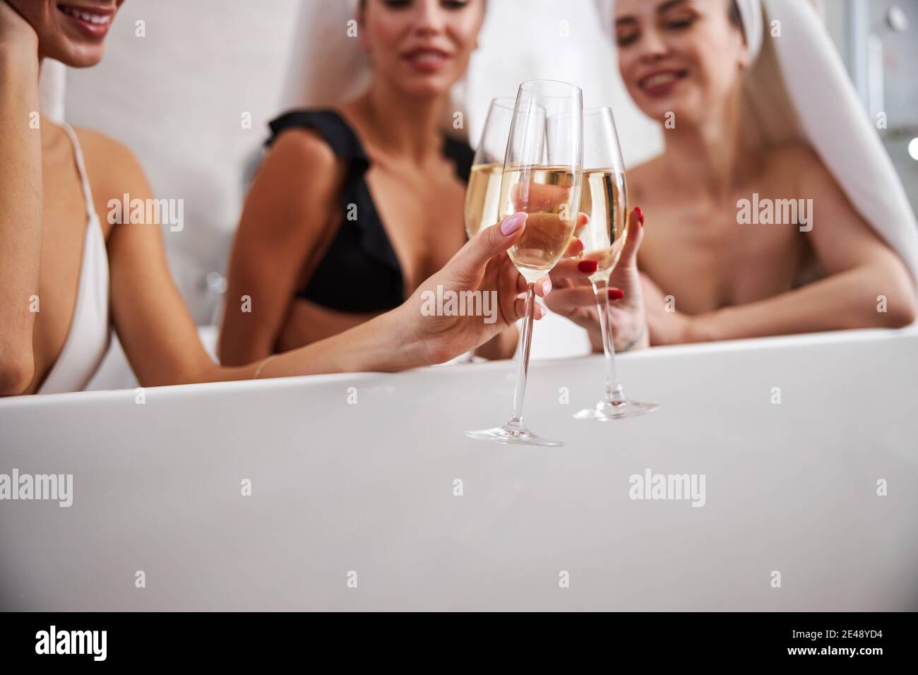 Junge Frauen laughng und trinken Champagner sitzen in der Badewanne Stockfoto