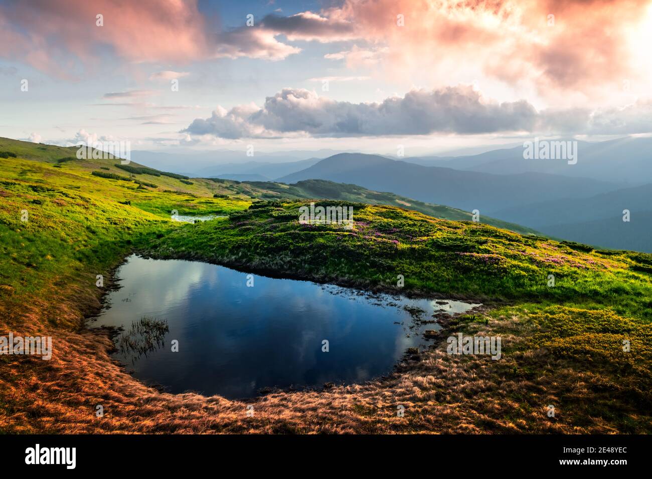 Bergsee bei Sonnenaufgang. Malerische Sommerlandschaft mit grünen Hügeln und Sonnenstrahlen am Morgenhimmel. Karpaten Stockfoto
