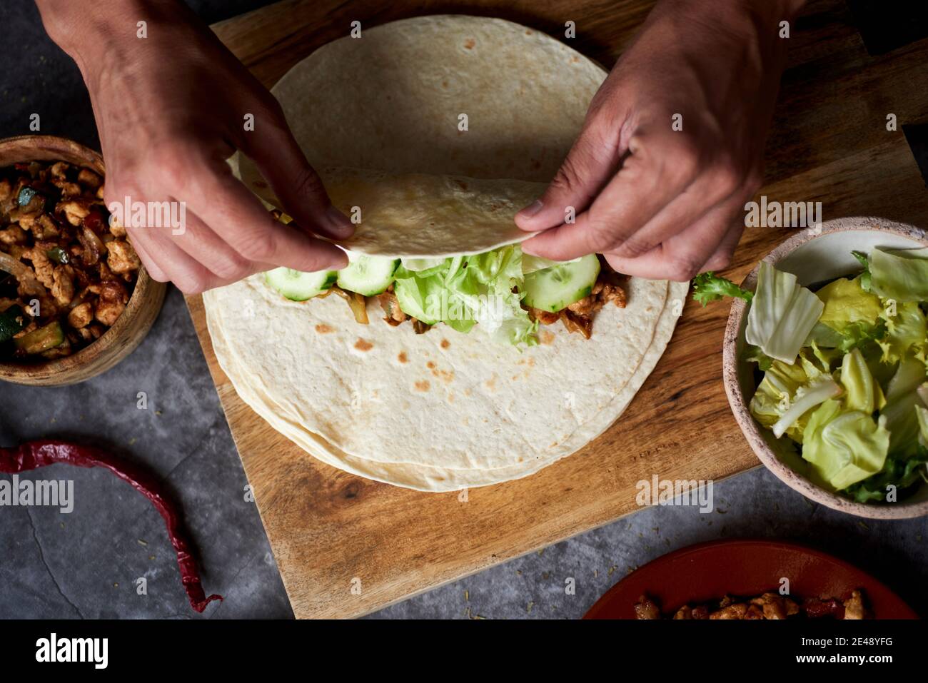 Blick aus dem hohen Winkel auf einen kaukasischen Mann, der ein Durum oder einen Burrito rollt, gefüllt mit Hühnerfleisch, das mit verschiedenen Gemüsesorten wie Zwiebeln oder roten und gr Stockfoto