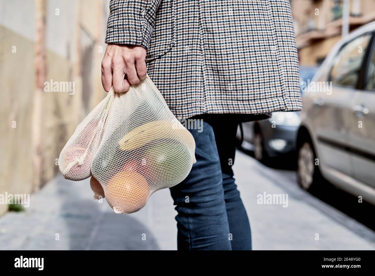 Ein Mann auf der Straße, von hinten gesehen, trägt einen wiederverwendbaren Textilbeutel, der verwendet wird, um Lebensmittel in großen Mengen zu kaufen, voller Obst und Gemüse, als Maßnahme Stockfoto