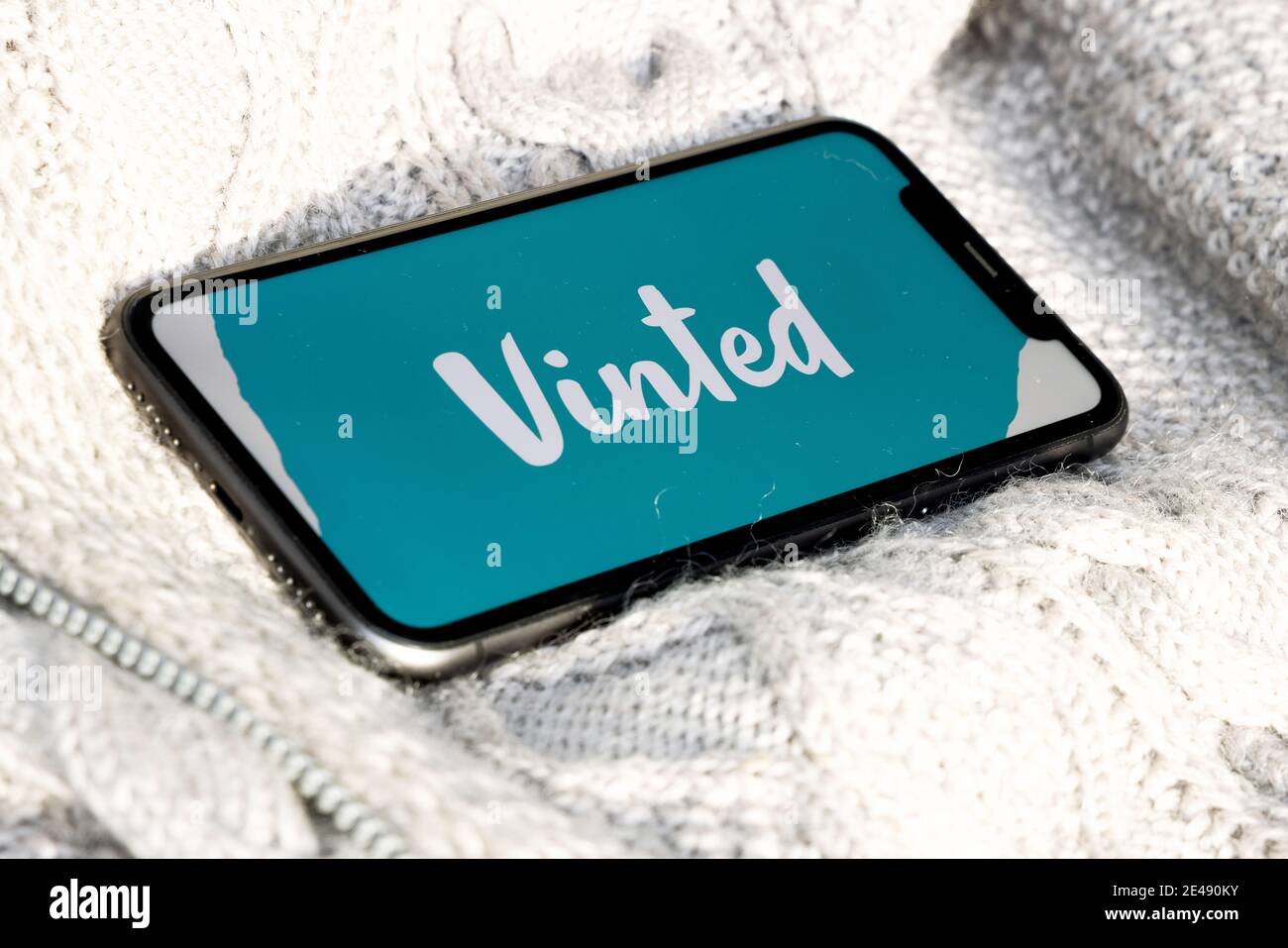 IPhone mit getöntem Logo auf dem Bildschirm auf Vintage-Strickstoff. Vinted ist ein litauischer Online-Marktplatz und eine Community für Second Hand Kleidung Stockfoto