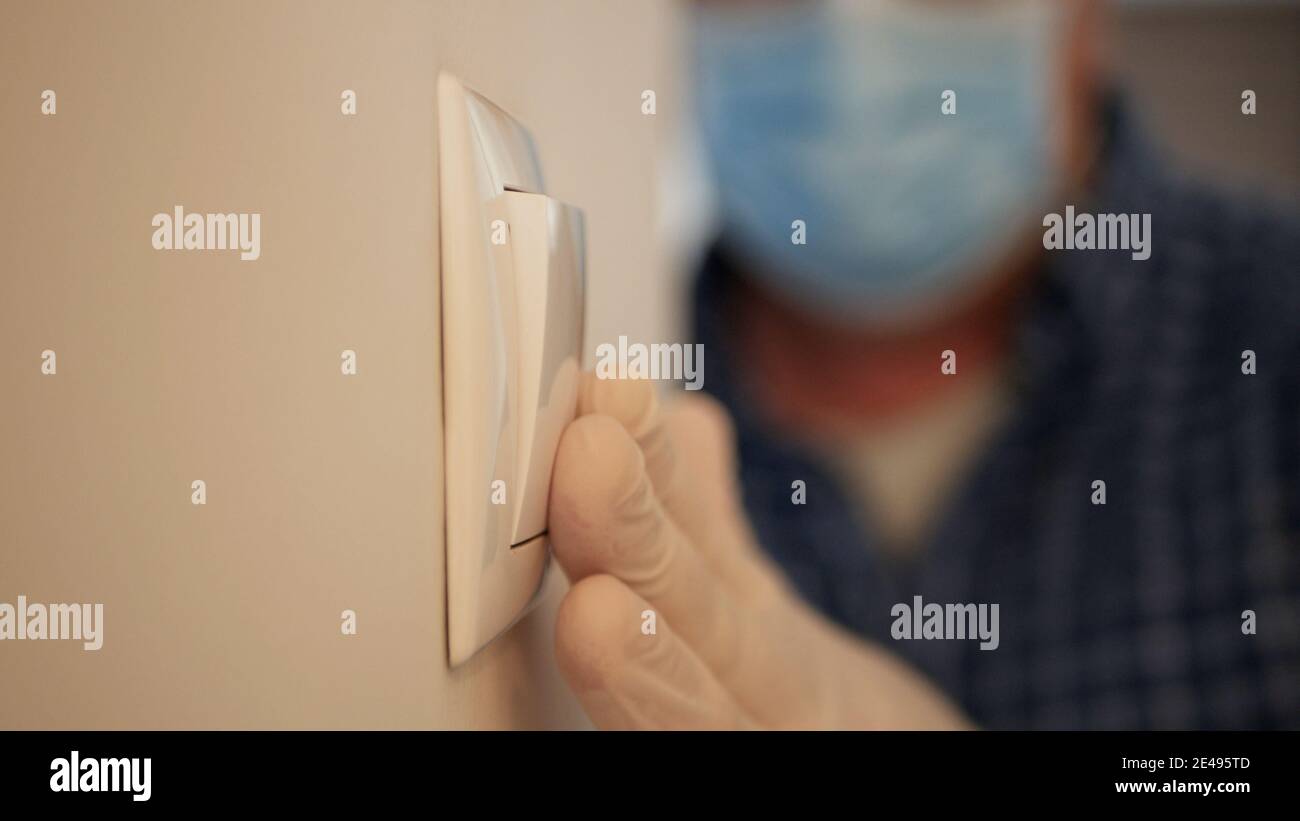 Mann trägt medizinische Maske und Schutzhandschuhe Betreten Sie den Büroraum und schalten Sie das Licht aus dem Schalter, Arbeitsplatz Quarantäne in Pandemie. Stockfoto