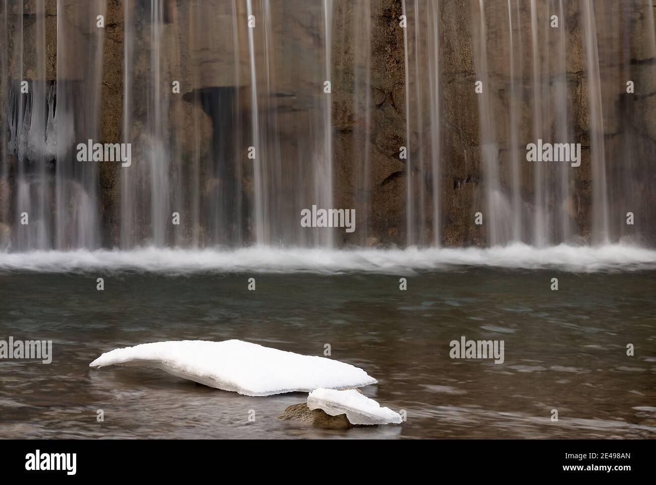 Verschwommenes Wasser, das aus einer Kaskade in einem Bach fällt. Mit Eis im Vordergrund. Stockfoto