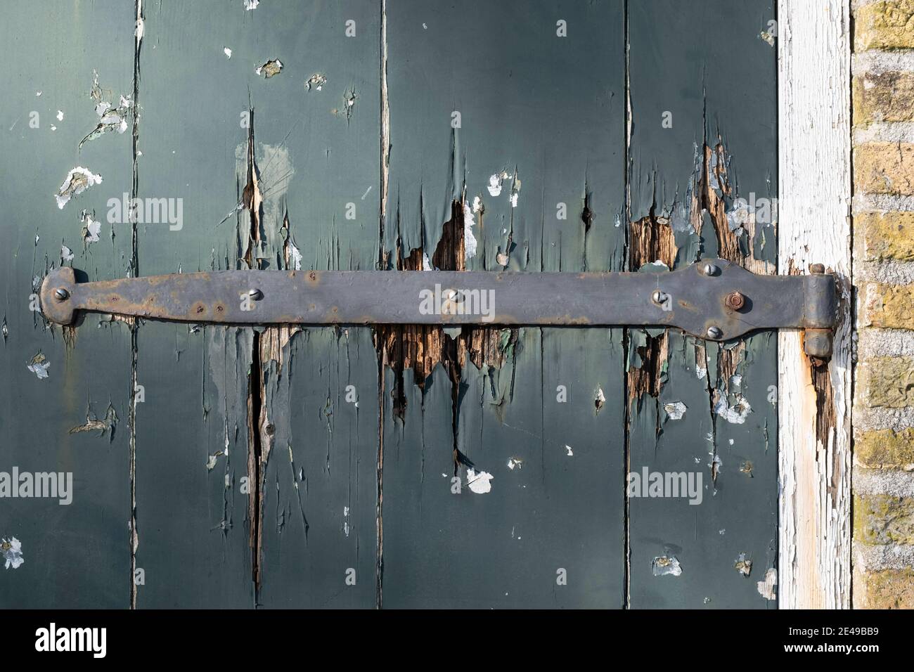 Langes antikes Metallscharnier an einer alten Tür mit abgebrochenen Malen Sie in einem weißen Rahmen neben einer Wand von Typisch holländische gelbe Ziegel Stockfoto