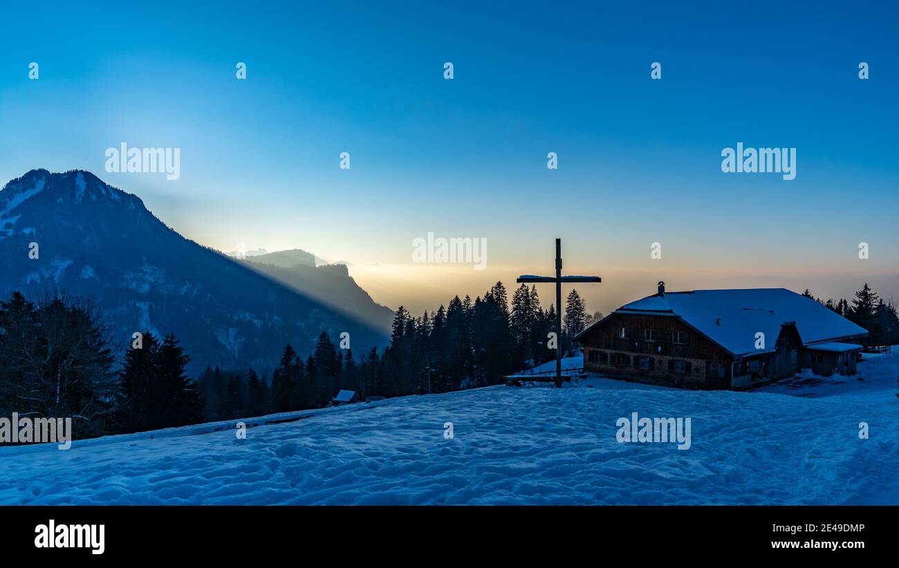 Kreuz auf dem verschneiten Hügel, Almwiesen mit Kreuz. Kreuz auf einer Alp bei Kehlegg, Dornbirn. Winter in österreichischen alpen, verschneite Berge bei Sonnenuntergang. Stockfoto