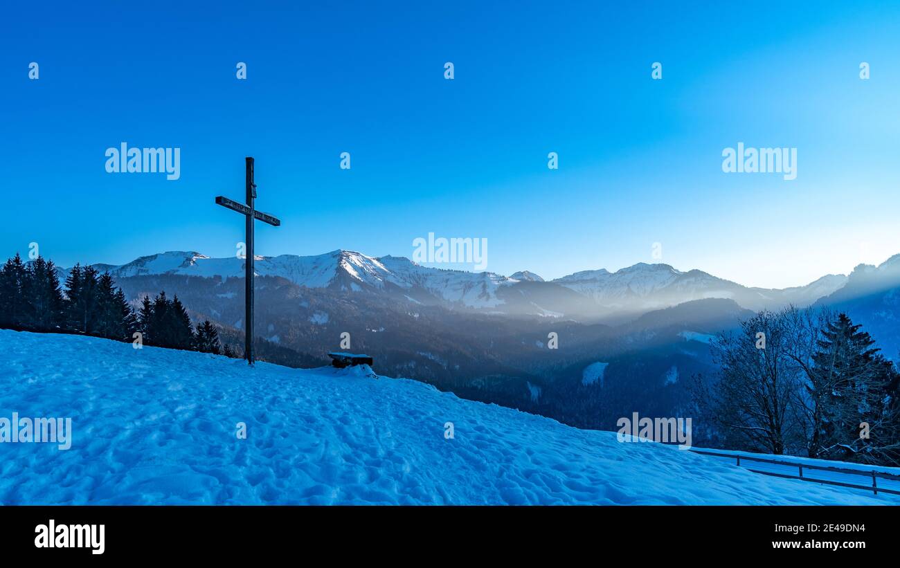 Kreuz auf dem verschneiten Hügel, Almwiesen mit Kreuz. Kreuz auf einer Alp bei Kehlegg, Dornbirn. Winter in österreichischen alpen, verschneite Berge bei Sonnenuntergang. Stockfoto