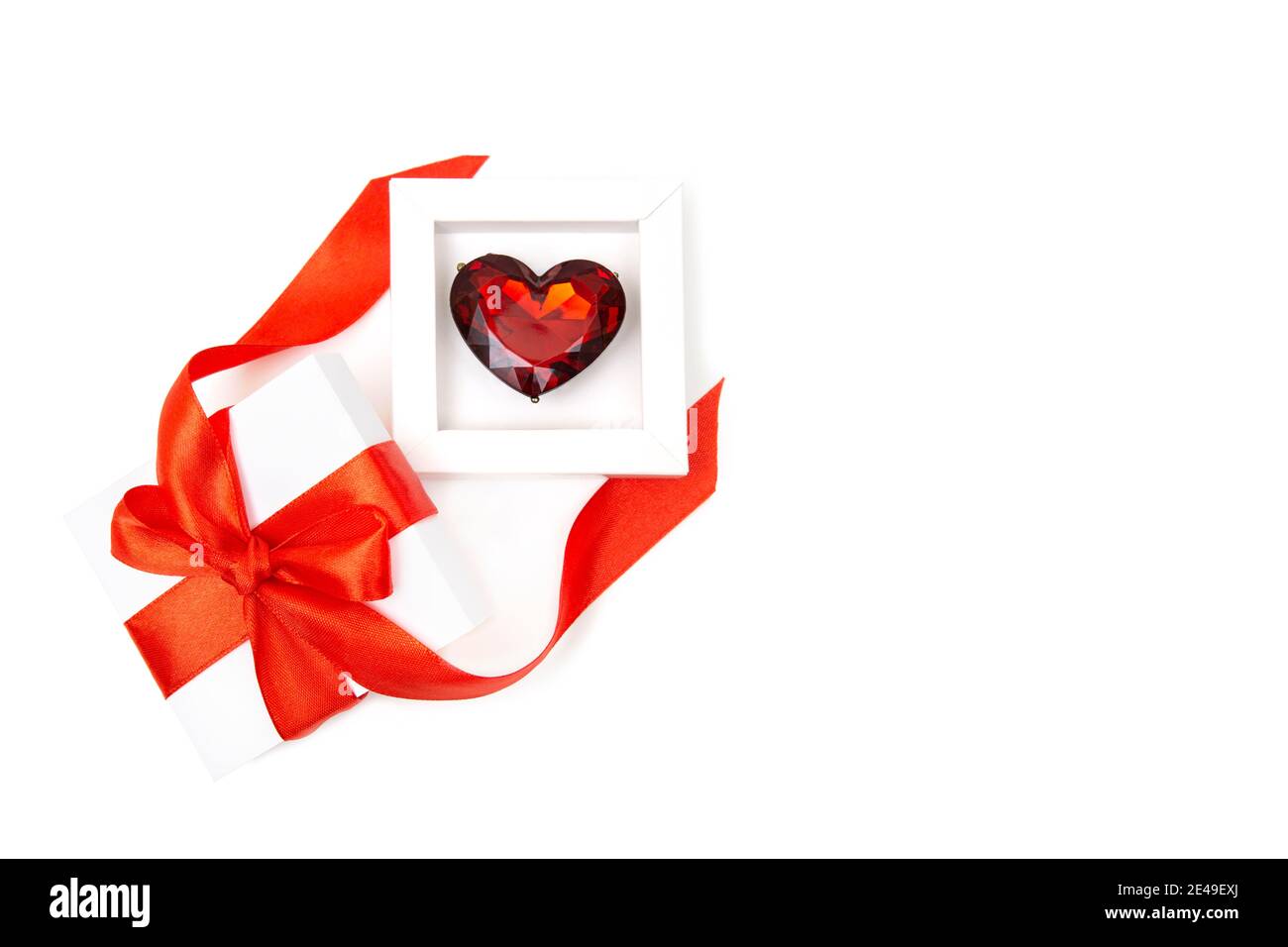 Großer rubinfarbener herzförmiger Ring in einer weißen Box mit einer roten Schleife und Band isoliert auf Weiß. Romantisches Geschenkkonzept zum Valentinstag. Stockfoto