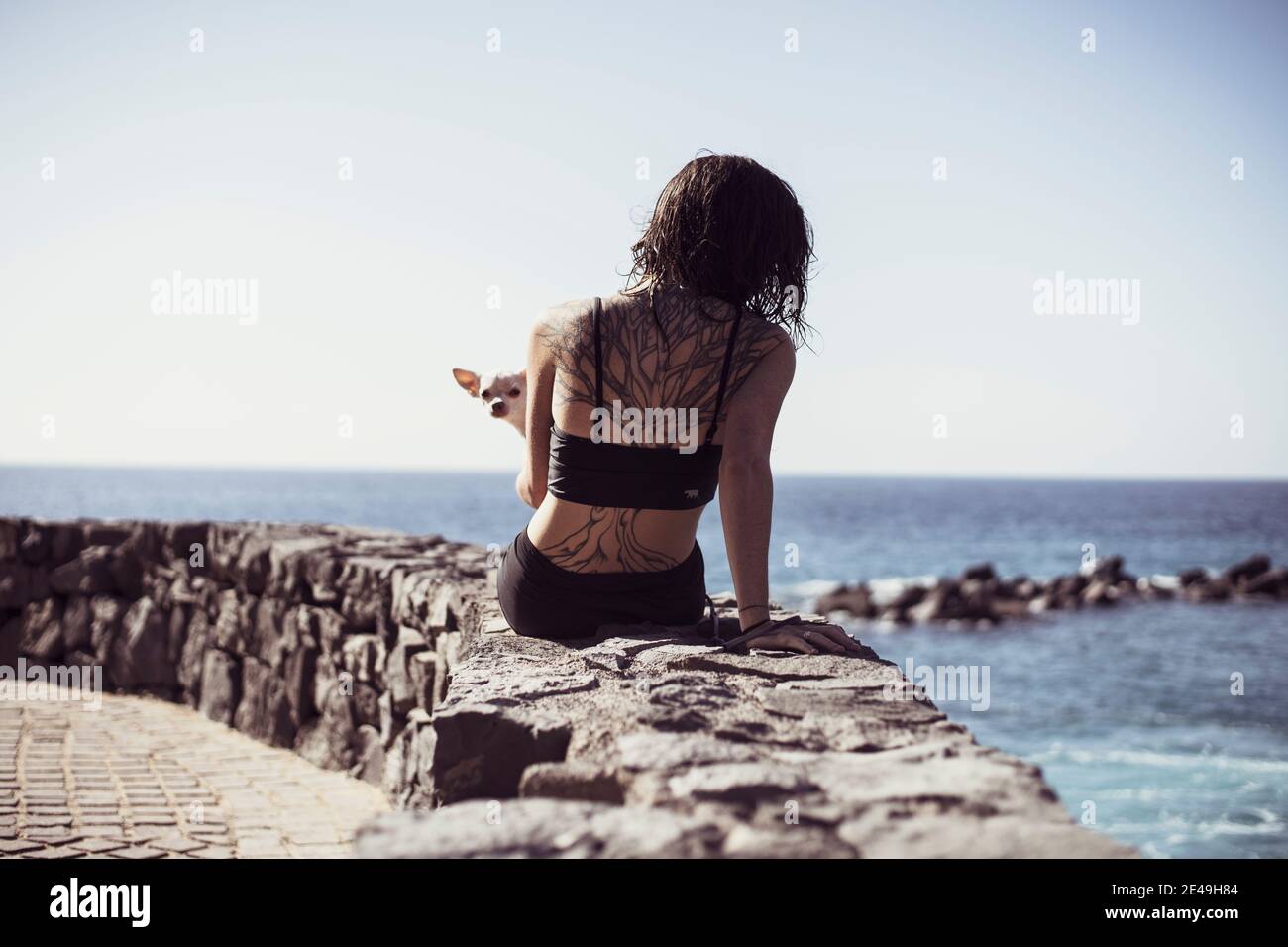 Fit Frau mit Baum Tattoo sitzt am Rande des Ozeans Mit niedlichem Hund auf dem Schoß Stockfoto